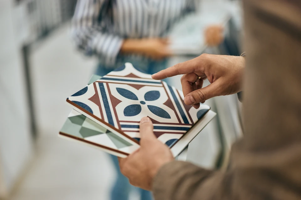 Photographie réaliste montrant un carreleur professionnel en train d'appliquer du mortier sur un mur intérieur à l'aide d'une truelle, préparant la pose de carrelage. L'artisan porte des vêtements de travail appropriés et est concentré sur sa tâche. L'arrière-plan montre un chantier de rénovation de salle de bain ou d'intérieur, avec des outils professionnels, des sacs de matériaux et une surface murale partiellement carrelée. L'image doit transmettre la rigueur, le savoir-faire technique et l'implication professionnelle d'un artisan maîtrisant son métier.